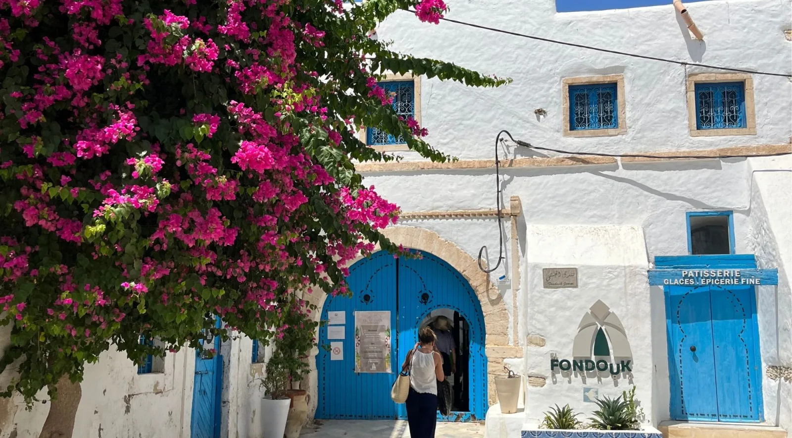A whitewashed Djerba street with cobalt-blue doors and bougainvillea in flower