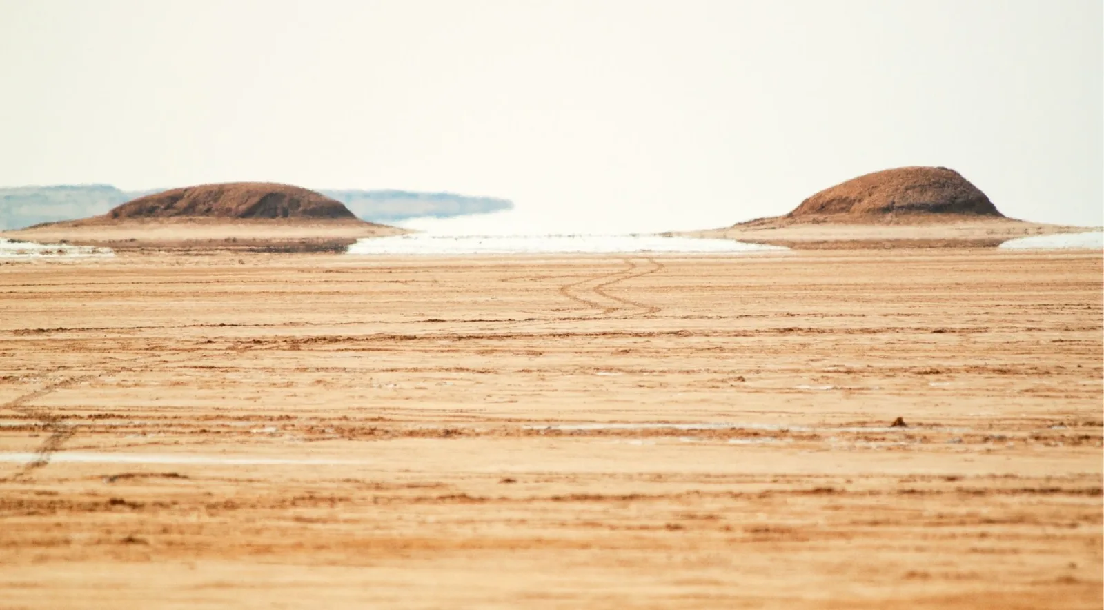 A pale salt flat with two low mounds breaking the horizon