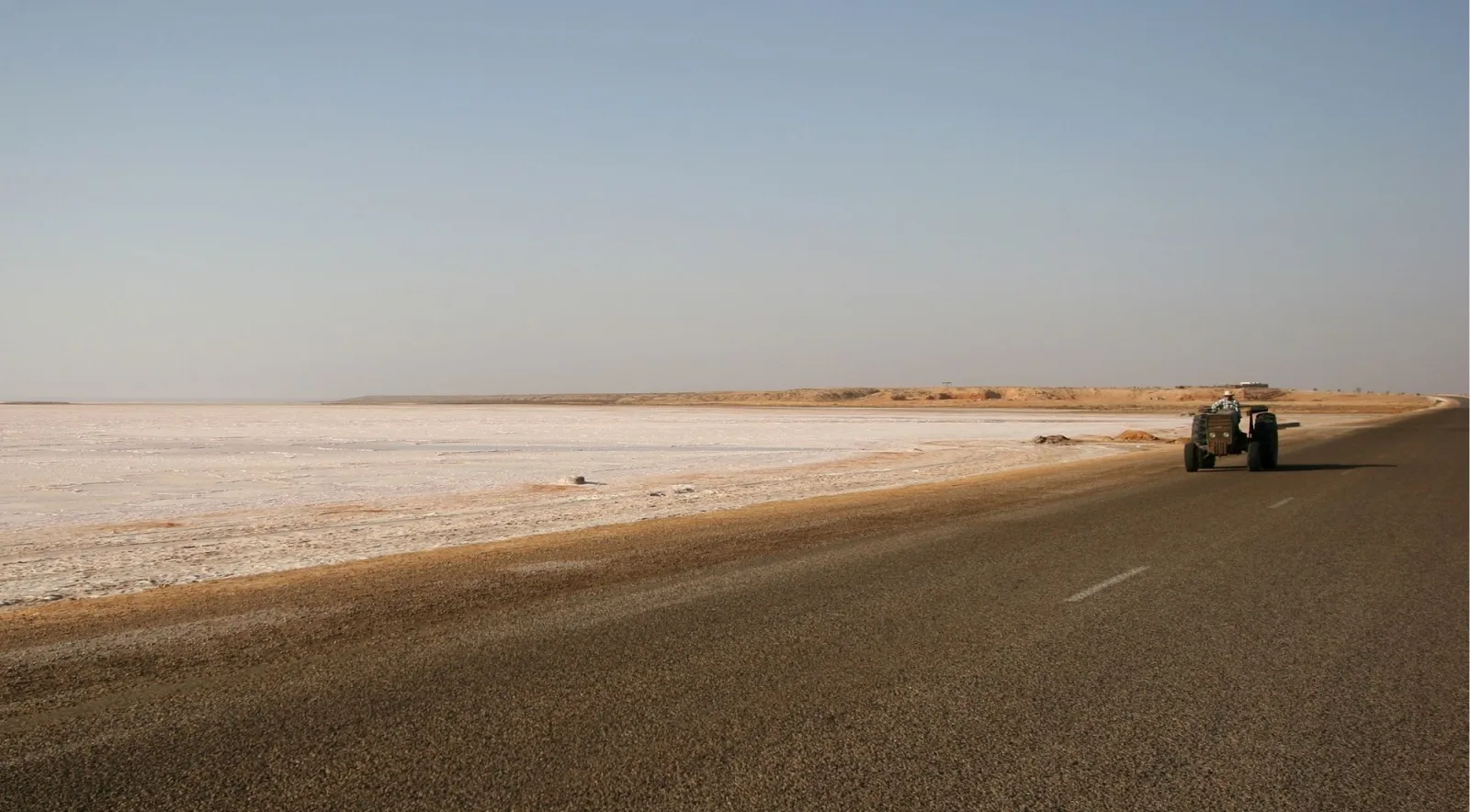 A straight road crossing a pale salt flat with a vehicle in the distance